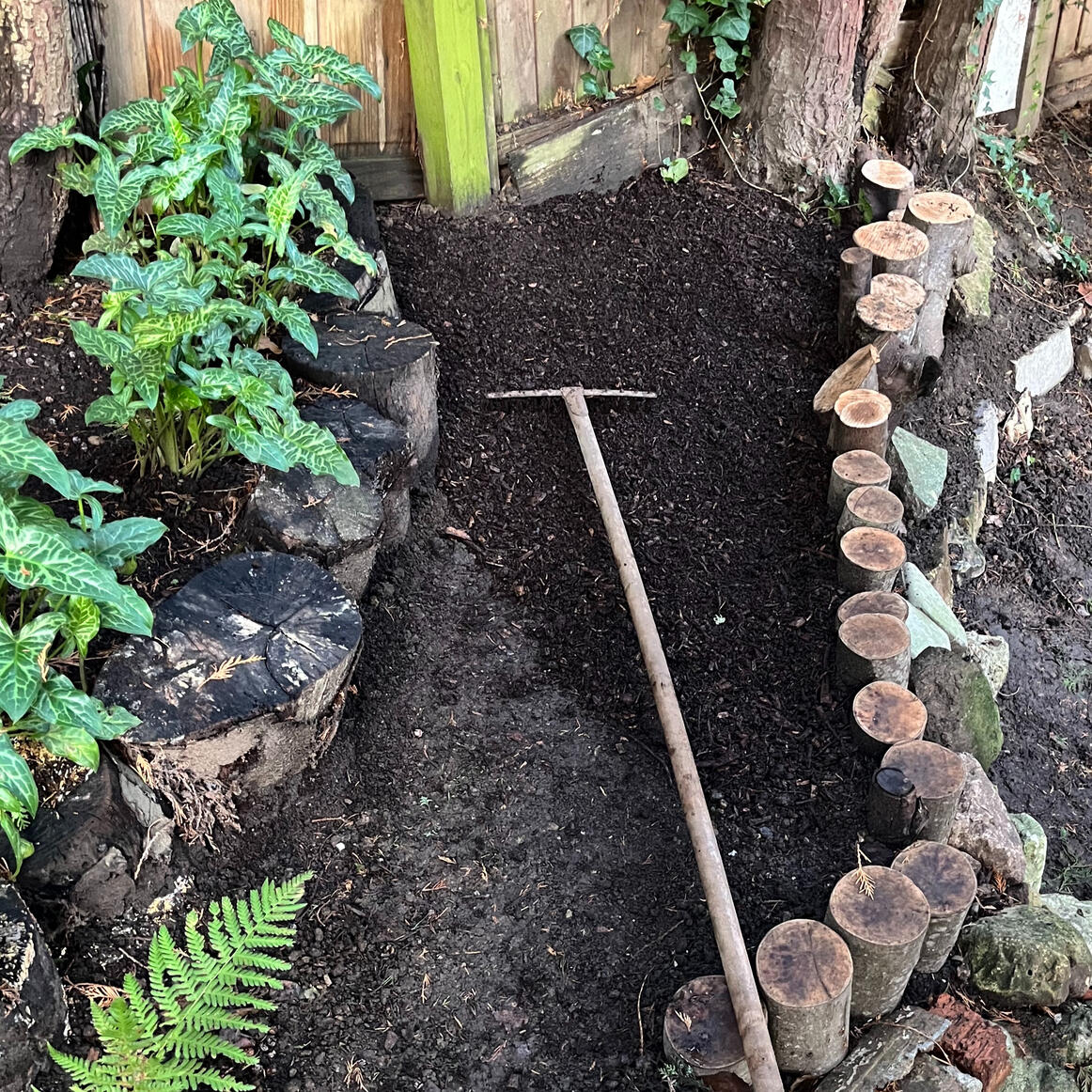 Photo of a tiered garden bed with newly fitted natural log edging, as mulch is being applied.
